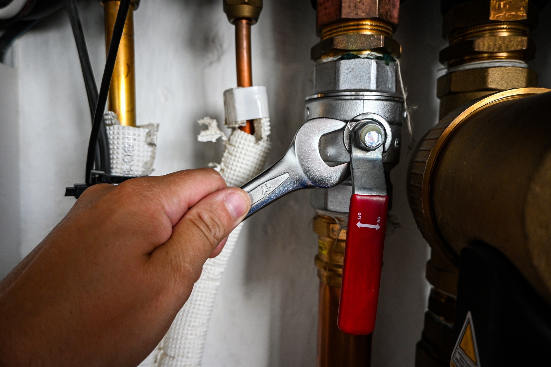 Plumber is tightening a nut on a water heater pipe using an adjustable wrench